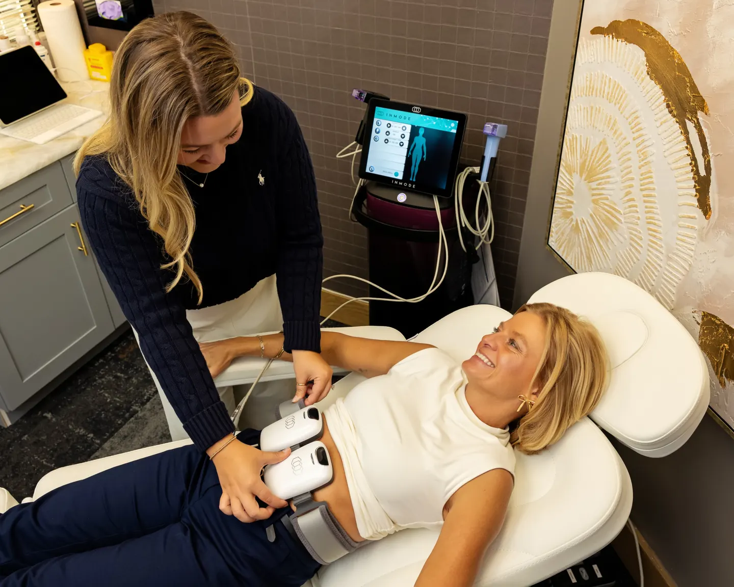 A provider fitting EMS muscle toning applicators across a reclining patient’s abdomen