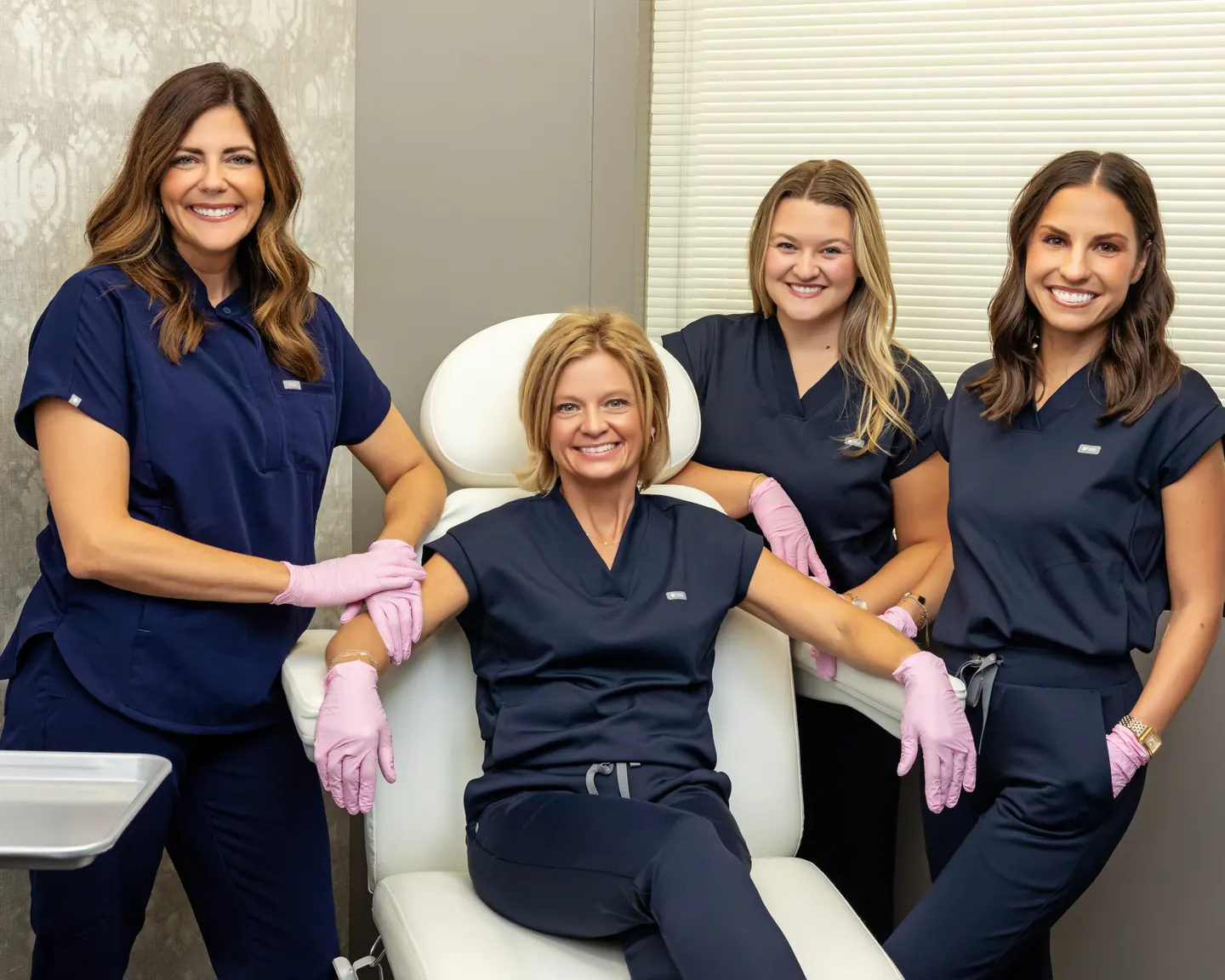 Four Premier Aesthetics team members in navy scrubs gathered around a treatment chair