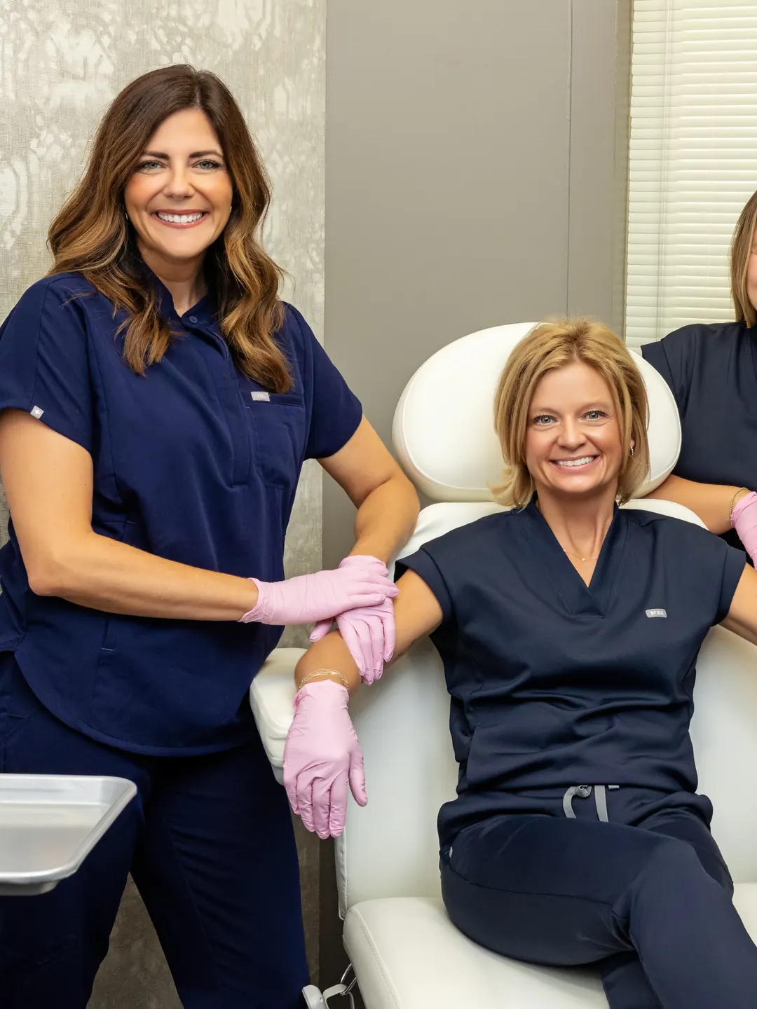 Two Premier Aesthetics team members in navy scrubs at a treatment chair